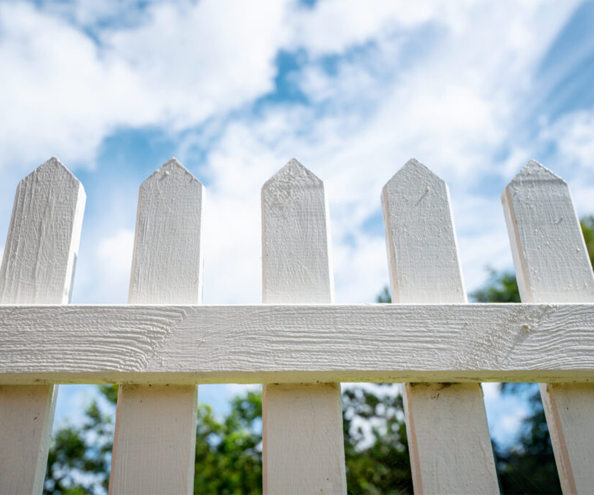 Classic white picket fence under a blue sky, showcasing timeless backyard fence design.