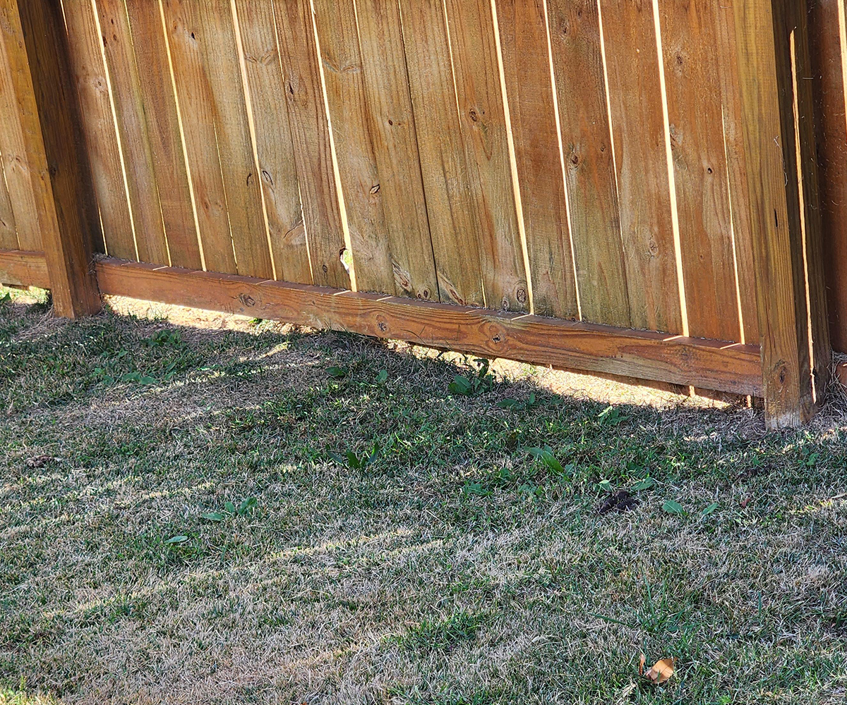 fence-contractor-sugarcreek-gaps-under-fence Warped wooden fence showing damage and need for repair by fence contractor Sugarcreek