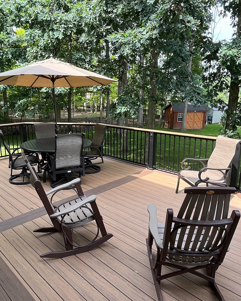 Buckeye-Elite-Decks-Custom-decks-in-Ohio Composite deck by deck builder in St. Clairsville with rocking chairs and dining set facing woods