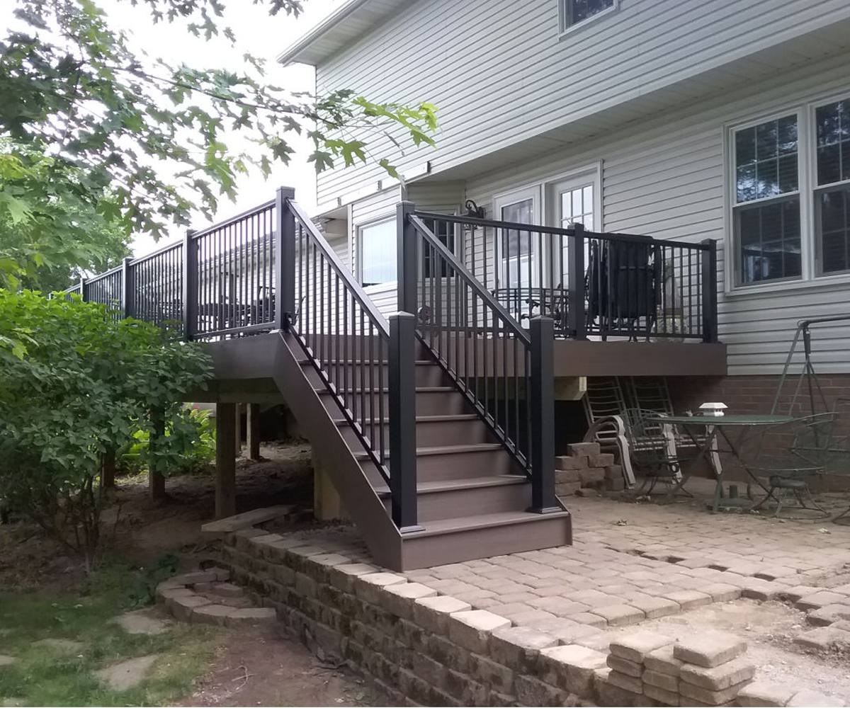 Backyard deck with black railing and staircase on tan vinyl-sided house
