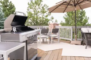 Outdoor kitchen and grill area on a deck with dining furniture and patio umbrella