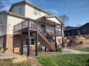 Raised backyard deck with black railings, covered landing, and a staircase leading to the patio.