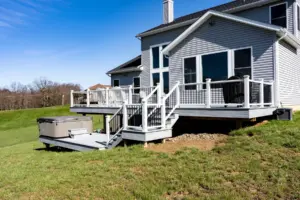 White composite deck with railing, stairs, and a hot tub overlooking an open backyard