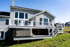 Elevated backyard deck with white railing, stairs, and a hot tub built beside the home