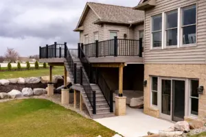 Elevated backyard deck with black railing, covered seating area, and stairs leading to a patio